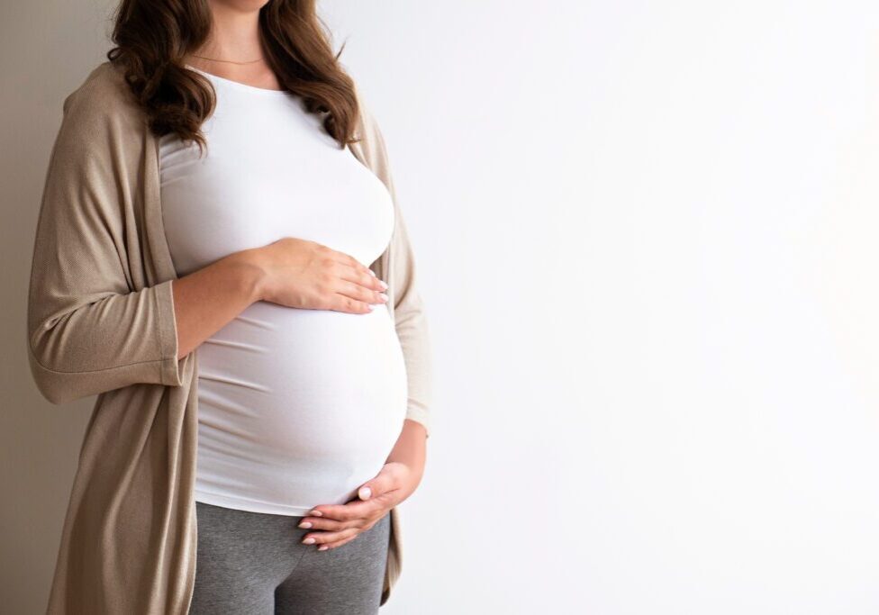Portrait shot of young beautiful woman on third trimester of pregnancy. Close up of pregnant female with arms on her round belly. Expecting a child concept. Background, copy space.