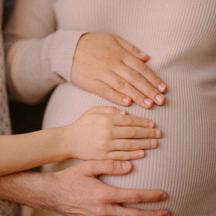 Family hands on pregnant surrogate during surrogacy journey